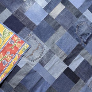 May include: A denim patchwork quilt in shades of blue, with a geometric design and denim pockets. A yellow and red floral patterned fabric is visible in the corner. The quilt is made from recycled denim.