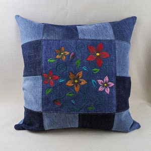 Puede incluir: Una almohada de mezclilla azul con un diseño de patchwork que presenta flores bordadas en tonos de rojo, naranja, rosa y amarillo.