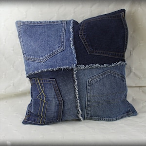 Puede incluir: Una almohada de mezclilla azul con diferentes tonos de mezclilla azul cosidos juntos en un diseño de patchwork. La almohada tiene un borde deshilachado y presenta múltiples bolsillos.