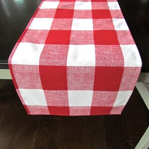 May include: Red and white checkered table runner. The runner is made of a woven fabric and has a slightly textured surface.