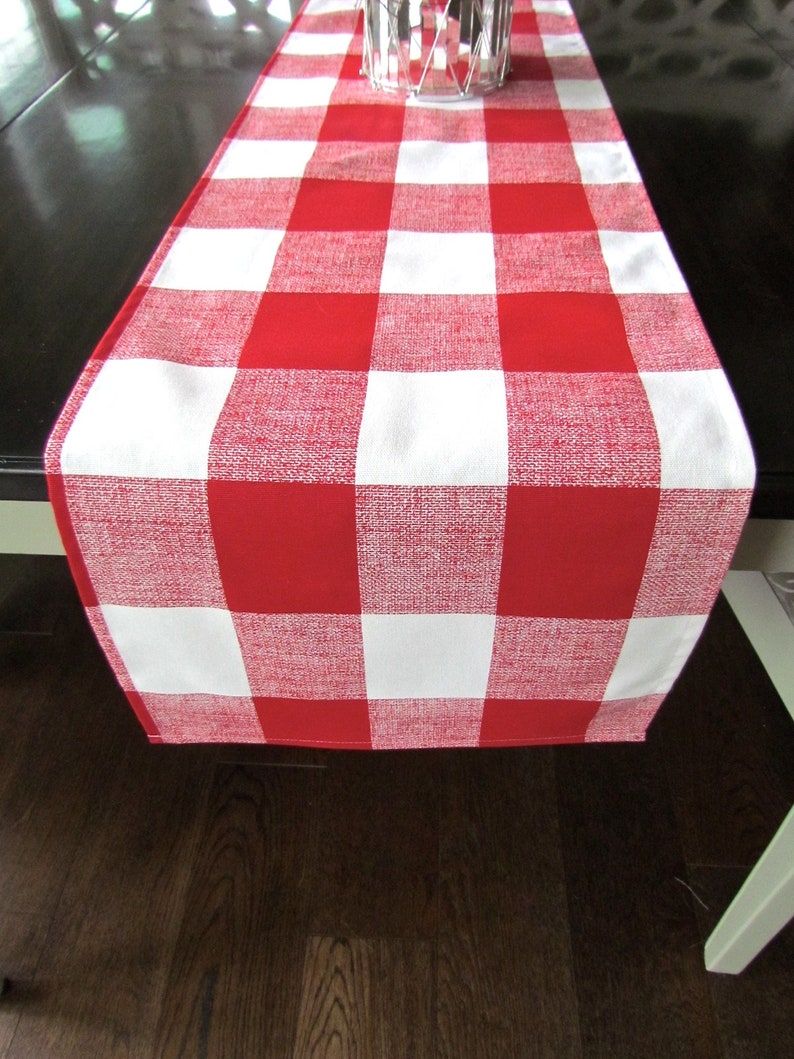 May include: Red and white checkered table runner. The runner is made of a woven fabric and has a slightly textured surface.