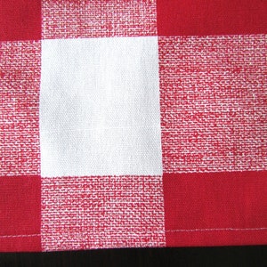 May include: Red and white checkered fabric with a white square in the center. The fabric has a woven texture.