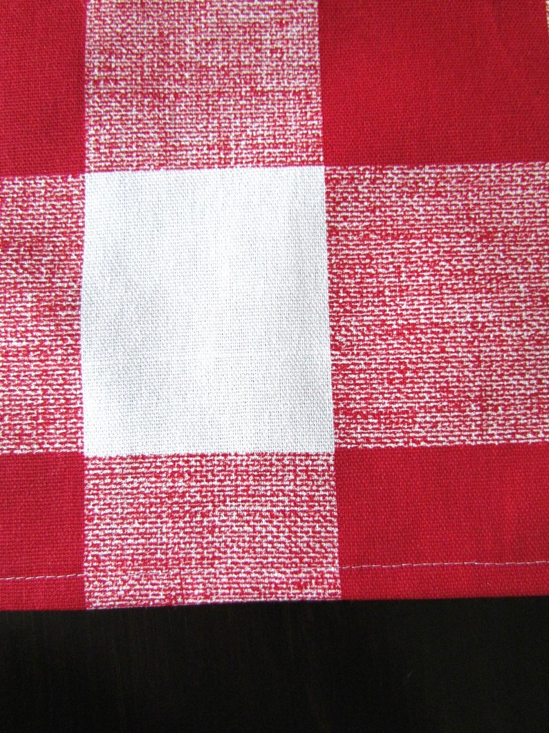 May include: Red and white checkered fabric with a white square in the center. The fabric has a woven texture.