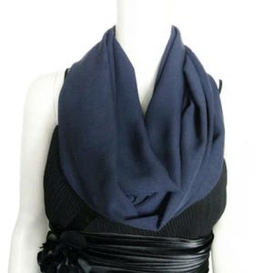 May include: A navy blue infinity scarf draped around a mannequin's neck. The scarf is made of a soft fabric and is styled over a black dress with a decorative floral accent at the waist. The scarf is a solid color and has a smooth texture.