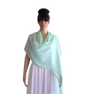 Könnte beinhalten: Ein hellgrüner Chiffon-Schal, der über ein weißes Kleid gelegt wird. Der Schal ist aus einem weichen, fließenden Stoff und hat ein schlichtes, elegantes Design.