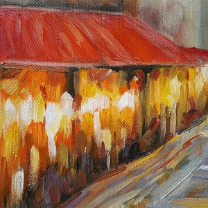 May include: Oil painting of a street scene with a red awning and buildings in warm tones of yellow, orange, and brown. The artwork has a textured, impressionistic style, with visible brushstrokes. A gray street is in the foreground.
