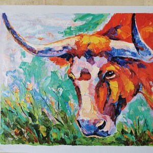 May include: An oil painting of a longhorn steer's head, rendered in vibrant, textured brushstrokes. The artwork features a palette of warm colors, including orange, red, and yellow, contrasted with cool blues and greens. The steer's face is white, and the horns are blue.