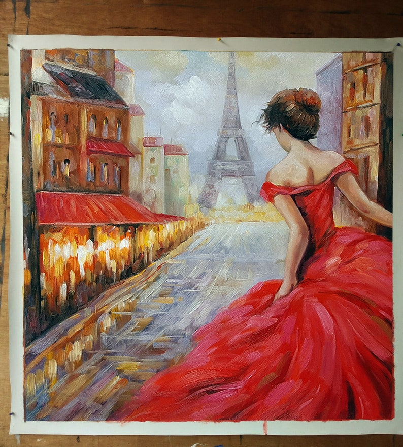 May include: Oil painting of a woman in a red dress walking down a Parisian street. The Eiffel Tower is visible in the background. Buildings with red awnings line the street. The artwork is on a white canvas.