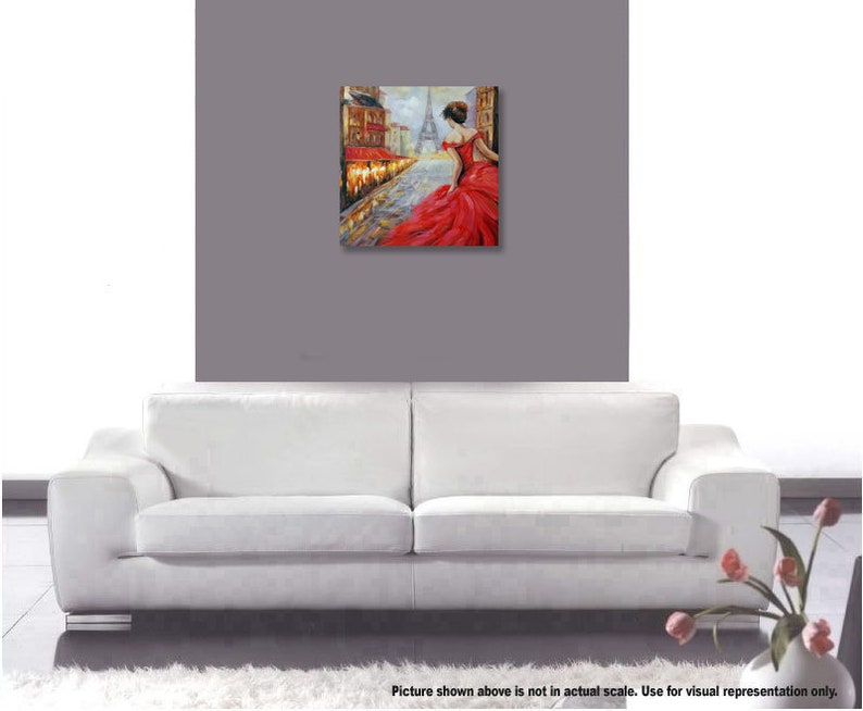 May include: An oil painting depicts a woman in a red dress walking on a cobblestone street in Paris. The Eiffel Tower is visible in the background. The artwork is displayed on a gray wall above a white sofa.