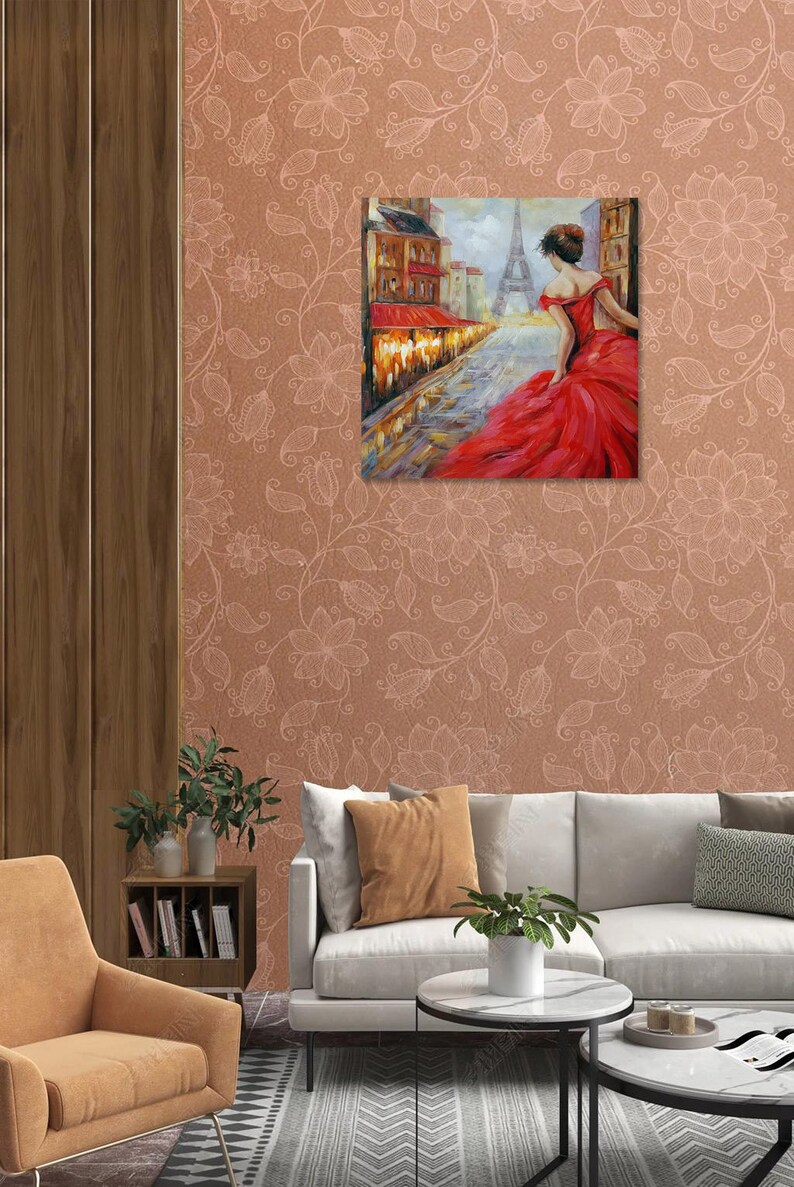 May include: A framed painting depicts a woman in a red dress walking down a Parisian street, with the Eiffel Tower in the background. The artwork is displayed on a floral patterned wall, above a sofa and chair. The room has a modern design.