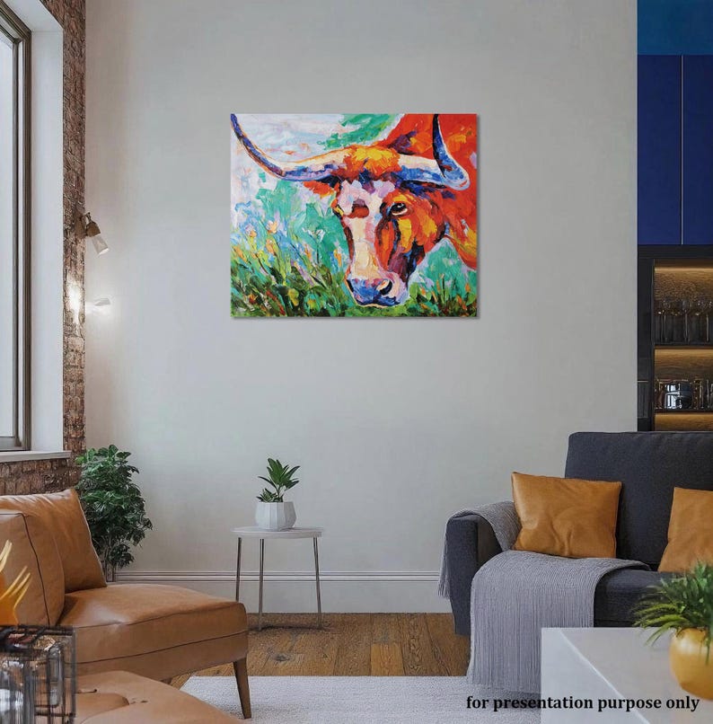 May include: A colorful painting of a longhorn bull's head. The artwork features vibrant hues of red, orange, yellow, and blue, with a green and white background. The bull's horns are long and curved. The painting is displayed on a wall in a living room.