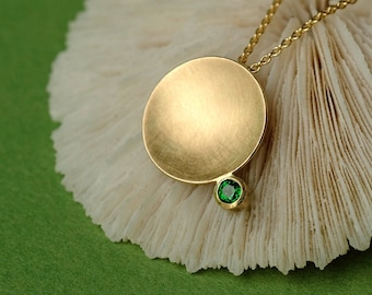May include: A gold necklace with a round pendant and a small green gemstone. The pendant is textured and has a smooth, rounded surface.