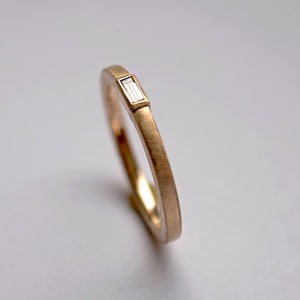 May include: A simple gold band ring with a small, rectangular diamond set in the centre.