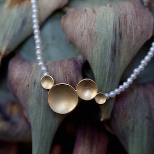 May include: A gold necklace with a cluster of round, textured, gold pendant charms. The necklace is made of small, white pearls.