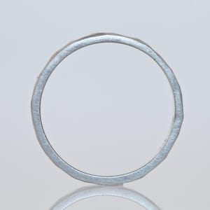 Może przedstawiać: Srebrny pierścionek o teksturowanym, młotkowanym wyglądzie. Pierścionek jest okrągły i wydaje się być wykonany z metalu. Design jest prosty i elegancki, odpowiedni do codziennego noszenia. Obręcz pierścionka ma szerokość około 0,2 cm.