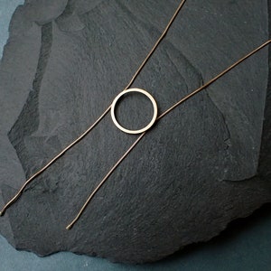 May include: A gold-toned necklace with a simple circle pendant. The necklace is on a dark gray background.