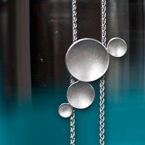 May include: A silver necklace with a chain and four round, silver pendants. The pendants are different sizes and are arranged in a cluster.