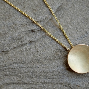 May include: A gold chain necklace with a round, smooth, gold pendant.