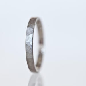 May include: A silver ring with a hammered texture. The ring is thin and has a slightly irregular surface, reflecting light. The ring is set against a white background.