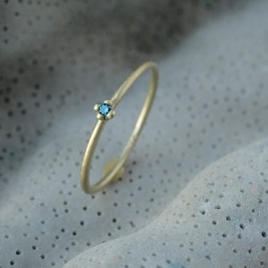 May include: A delicate gold ring with a single blue gemstone set in the center.