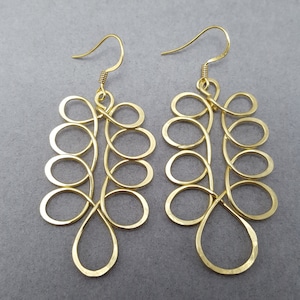 May include: A pair of gold-coloured earrings. Each earring is crafted from wire, featuring a series of connected loops and teardrop shapes, suspended from a simple hook. The design is symmetrical and has a delicate, open appearance.