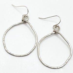 May include: A pair of silver teardrop earrings. The earrings have a hammered texture and are suspended from simple ear wires. The design is minimalist and modern, suitable for everyday wear or special occasions.