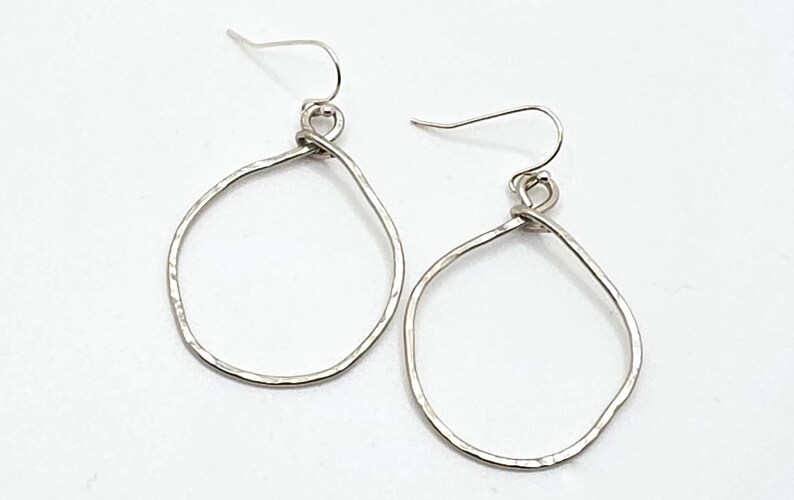 May include: A pair of silver teardrop earrings. The earrings have a hammered texture and are suspended from simple ear wires. The design is minimalist and modern, suitable for everyday wear or special occasions.