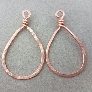 May include: Two copper-colored teardrop-shaped earring components. Each has a hammered texture and a loop at the top for attachment. The earrings are displayed against a neutral gray background.