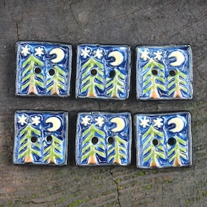 Puede incluir: Seis botones de cerámica azul con un diseño de dos pinos verdes, una luna creciente y estrellas blancas. Los botones tienen dos agujeros cada uno.