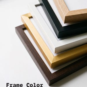 May include: A stack of five rectangular picture frames in varying finishes including light wood grain, matte black, white, metallic gold, and dark wood grain. The text Frame Color and FRAME COLOR MAY HAVE SLIGHT VARIANCES is printed below.