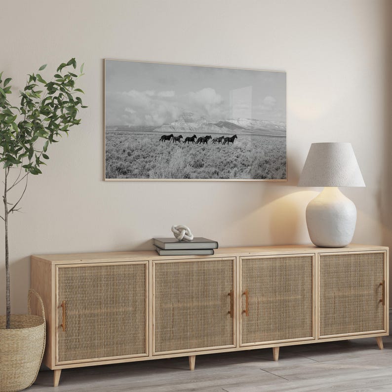 Puede incluir: Un armario de madera clara con cuatro puertas, cada una con un panel de rat&aacute;n tejido. El armario est&aacute; sobre un suelo de madera clara. Una fotograf&iacute;a en blanco y negro de caballos corriendo en un campo est&aacute; colgada en la pared sobre el armario. Una l&aacute;mpara de cer&aacute;mica blanca con una pantalla blanca est&aacute; a la derecha del armario.