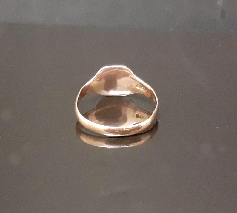 May include: A gold signet ring with a smooth, rounded top. The ring is made of a shiny metal and has a simple design.