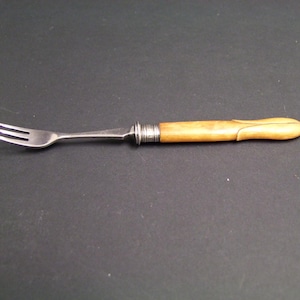 May include: A small silver-toned metal fork featuring three tines and a smooth, light tan, cylindrical handle with a carved, petal-like design at the end. A silver-coloured metal collar with horizontal ridges connects the handle to the fork head.