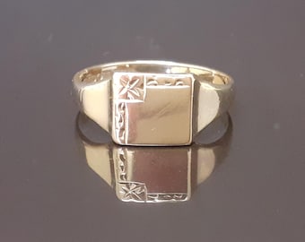 May include: A gold signet ring with a square, engraved top. The ring has a simple, classic design.