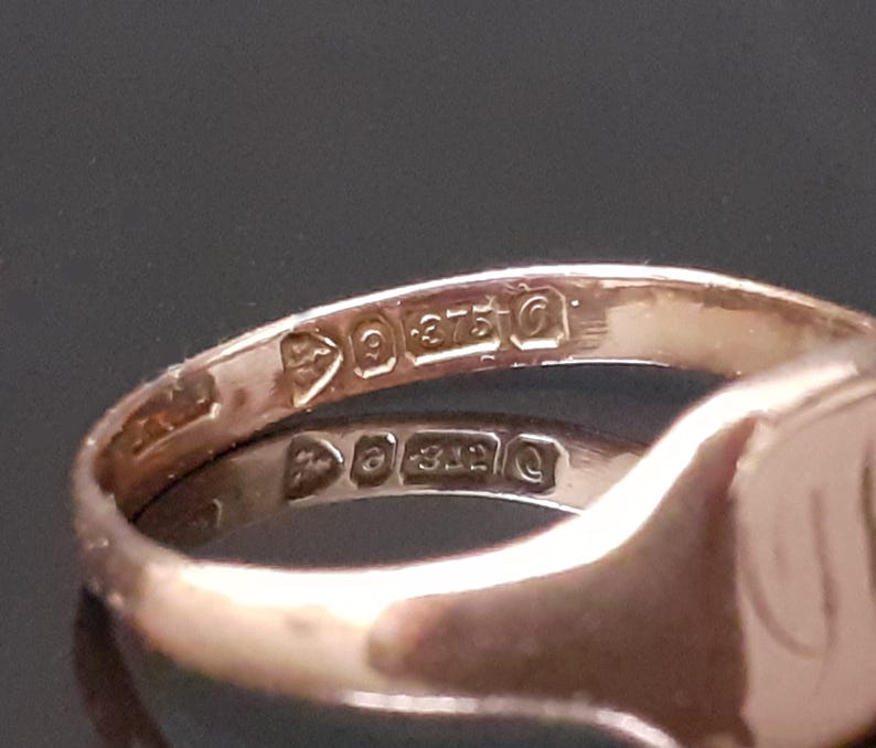 May include: Close-up of the inside of a gold signet ring with the inscription "9 375" on the band.