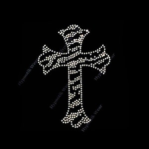May include: A silver rhinestone cross with a detailed design. The cross is on a black background.