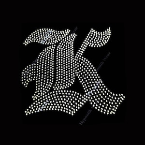 May include: A white rhinestone design of the letter K on a black background.