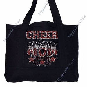 May include: Black canvas tote bag with the words "CHEER MOM" in red rhinestones. The letters are outlined in white rhinestones. There are five red stars with white rhinestone outlines below the words.