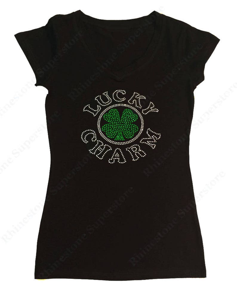 Puede incluir: Camiseta negra con un dise&ntilde;o de pedrer&iacute;a que dice "Lucky Charm" con un tr&eacute;bol de cuatro hojas verde en el centro.