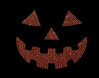 May include: Orange and yellow jack-o'-lantern face made of rhinestones on a black background.