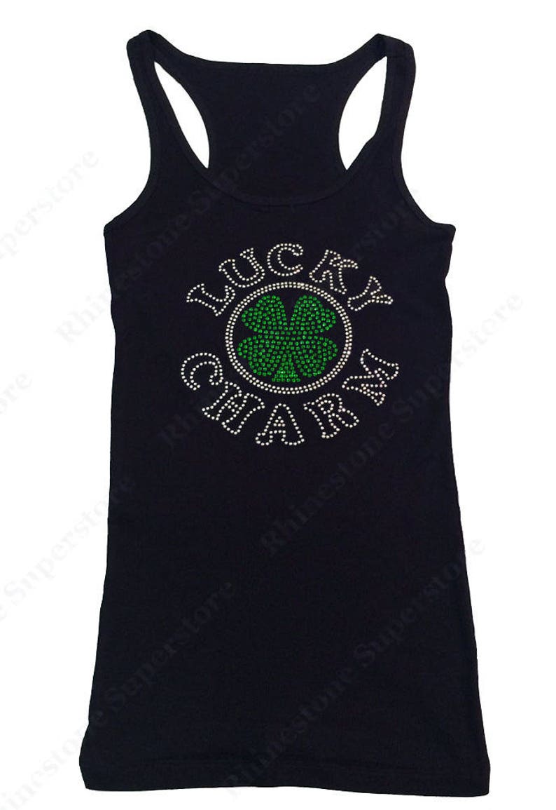 Puede incluir: Camiseta de tirantes negra con un dise&ntilde;o de pedrer&iacute;a que dice "Lucky Charm" con un tr&eacute;bol de cuatro hojas verde en el centro.