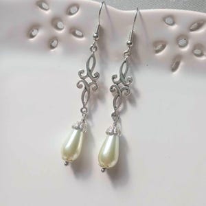 May include: A pair of silver dangle earrings with a delicate filigree design and a single white pearl drop on each earring.