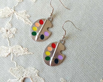 May include: A pair of silver earrings with a paint palette design. Each palette features six colorful paint wells and a silver paintbrush.