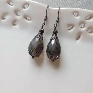 May include: A pair of dangle earrings with a teardrop-shaped grey glass bead and a black metal setting.