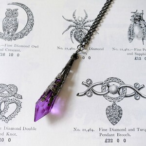A handmade transparent purple and gunmetal coloured ornate metal and acrylic drop bead pendant necklace on chain lying on an antique jewellery catalogue page