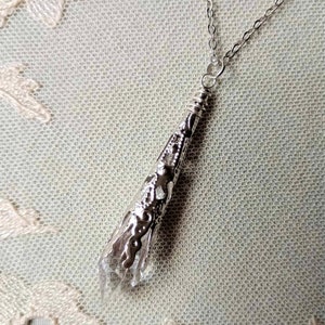 Op de afbeelding: Een zilveren ketting met een heldere kristallen hanger ingekapseld in een filigraan zilveren ontwerp.