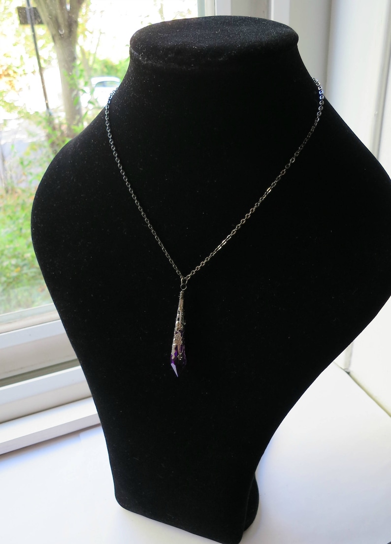 Pu&ograve; includere: Una collana con catena d'argento con un ciondolo a forma di cristallo viola lungo e appuntito.