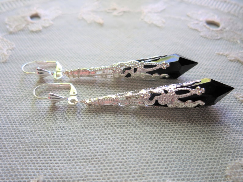 A pair of handmade jet black and bright silver coloured ornate metal and acrylic long drop bead leverback earrings lying on a cream lace doily
