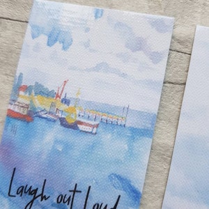 May include: A watercolour painting of a harbour scene with boats and a crane. The sky is blue with white clouds. The text "Laugh out Loud" is written in black at the bottom of the image.