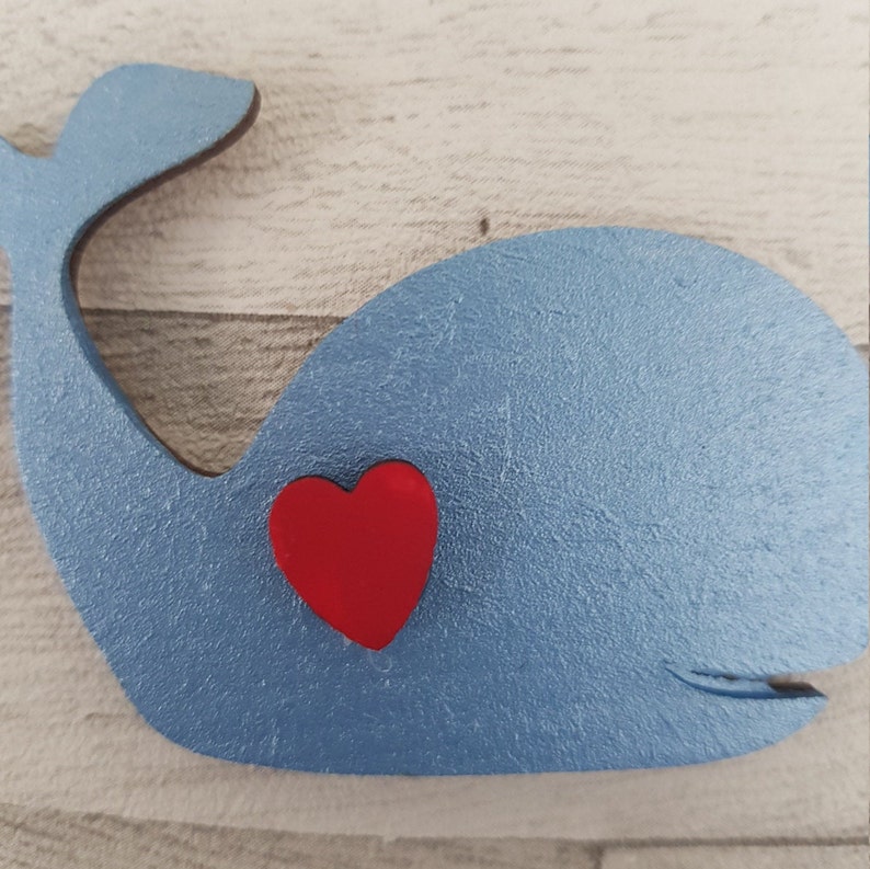 K&ouml;nnte beinhalten: Ein blauer Wal aus Holz mit einem roten Herzen in der Mitte. Der Wal ist hellblau bemalt und das Herz ist leuchtend rot.